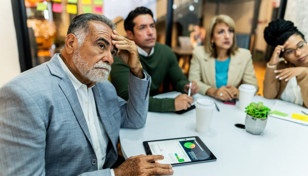 Worried senior businessman listening presentation with coworkers during business meeting at office